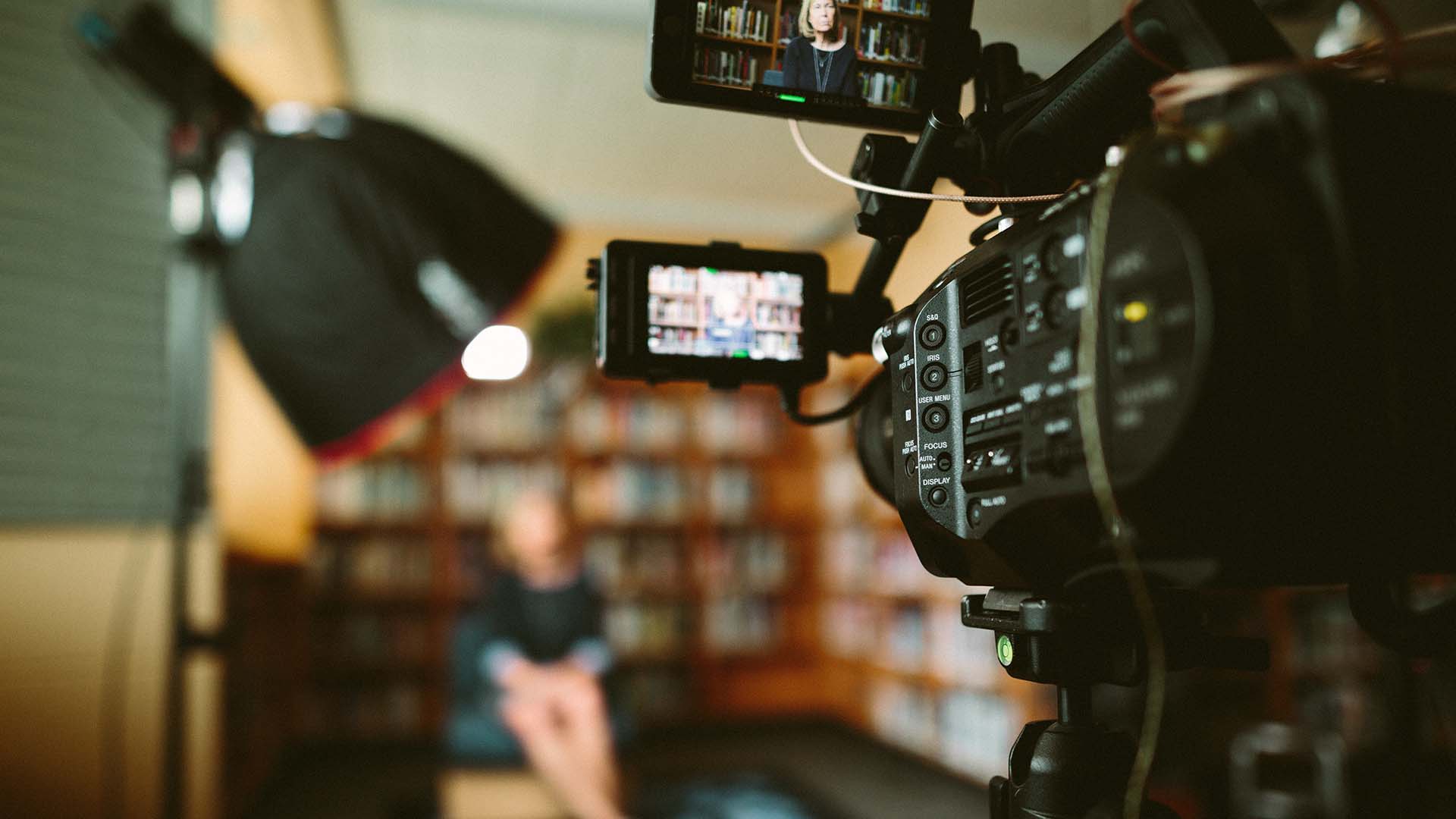 Closeup of camera in a library filming an interview of a woman