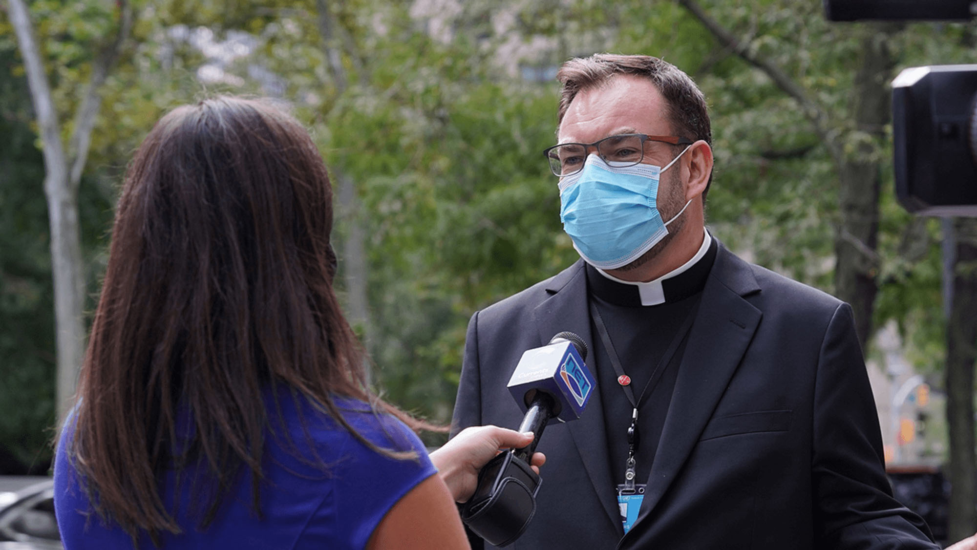 News reporter interviewing a clergyman who is wearing a mask
