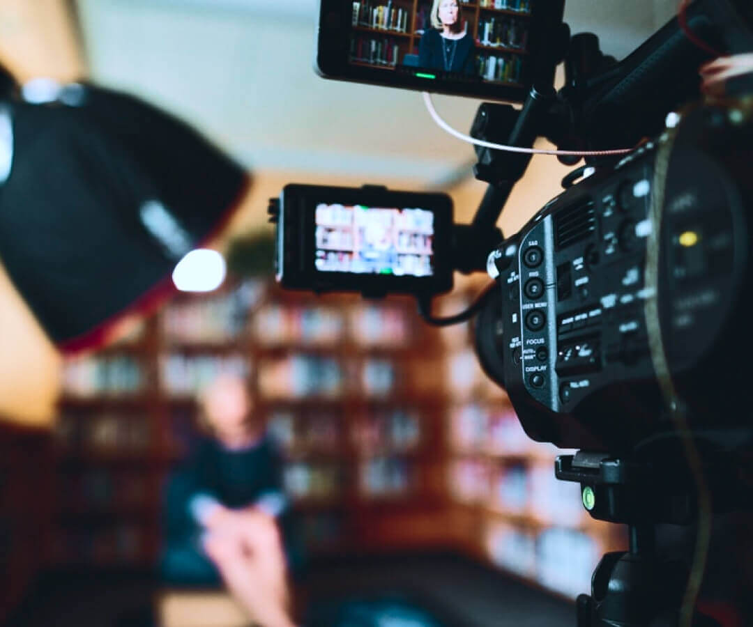 Closeup of camera in a library filming an interview of a woman