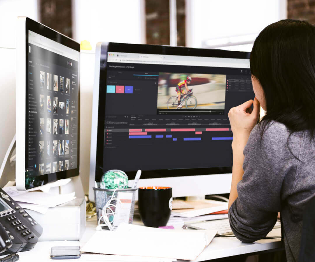 Woman at desk with two computer screens editing a video project